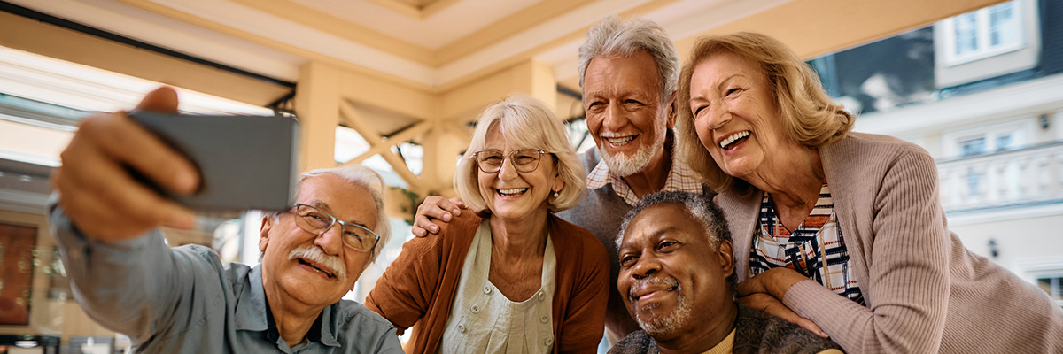 Multiracial group of happy senior people taking selfie with cell phone in nursing home